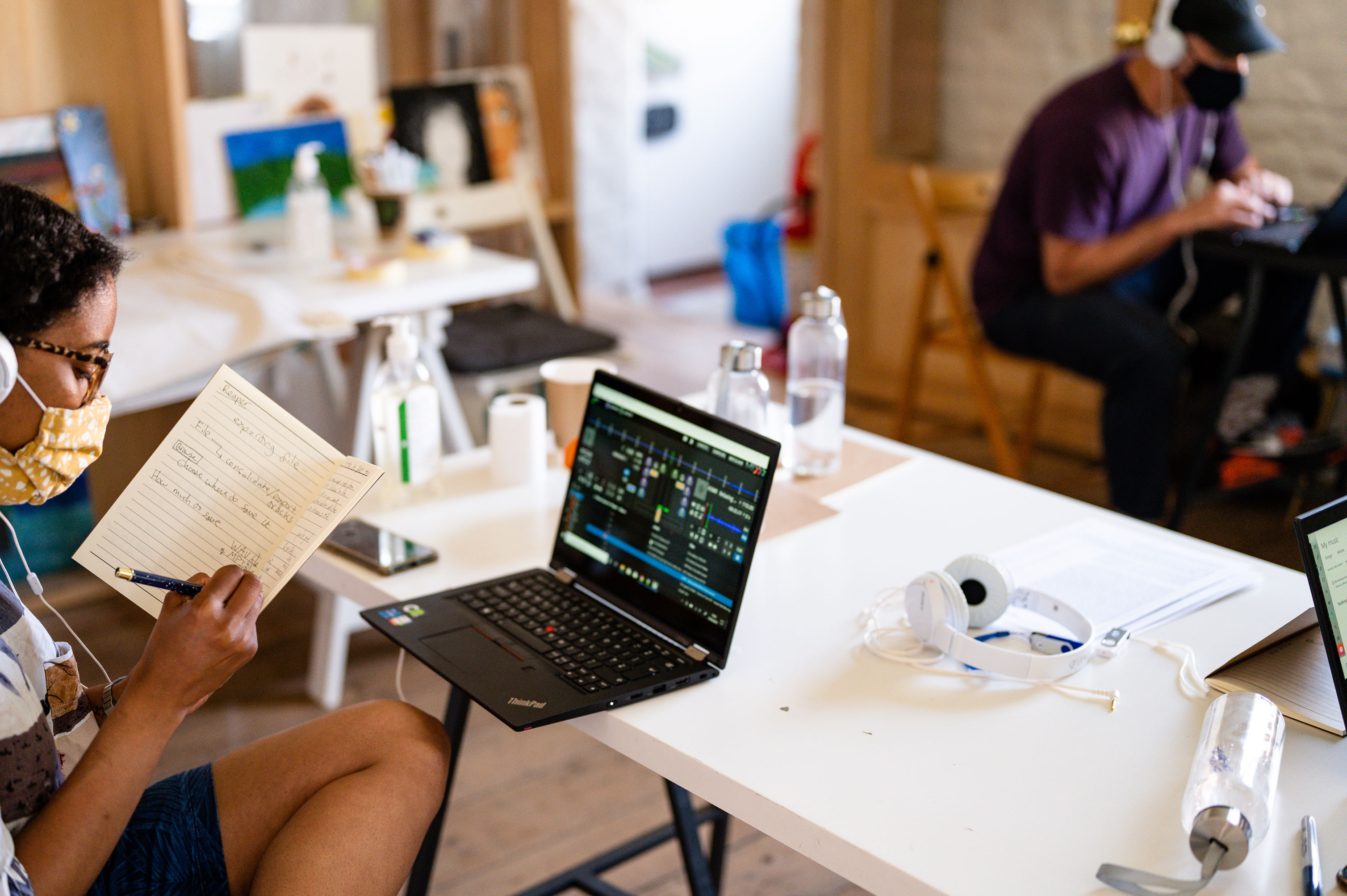 A participant writing notes in a notebook whilst sitting at a table with a laptop and headphones