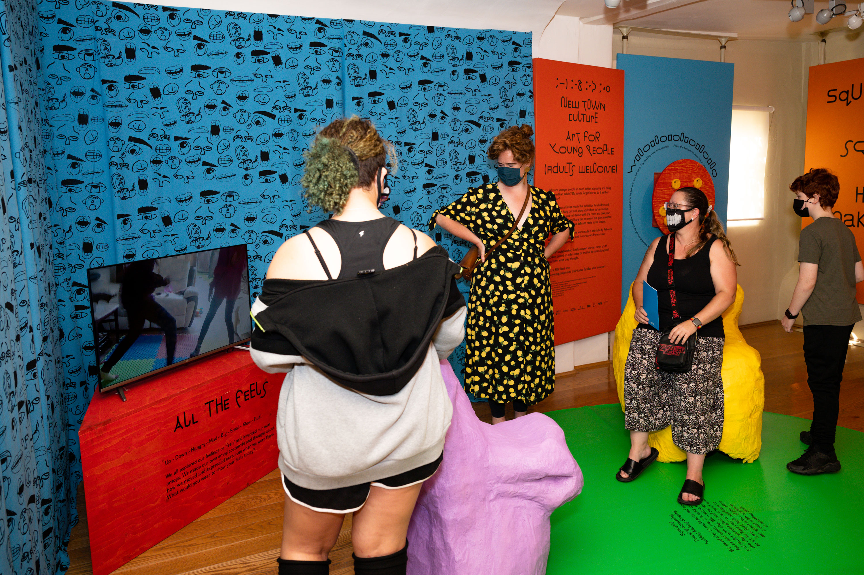 Two adults and two children looking at the art film on a screen placed on a red plinth