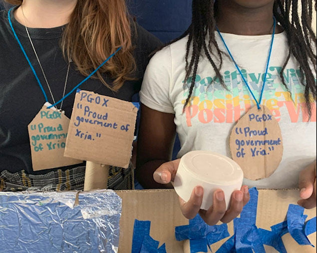 Moving Image still of two young women holding a sculpture and cardboard signs and banners