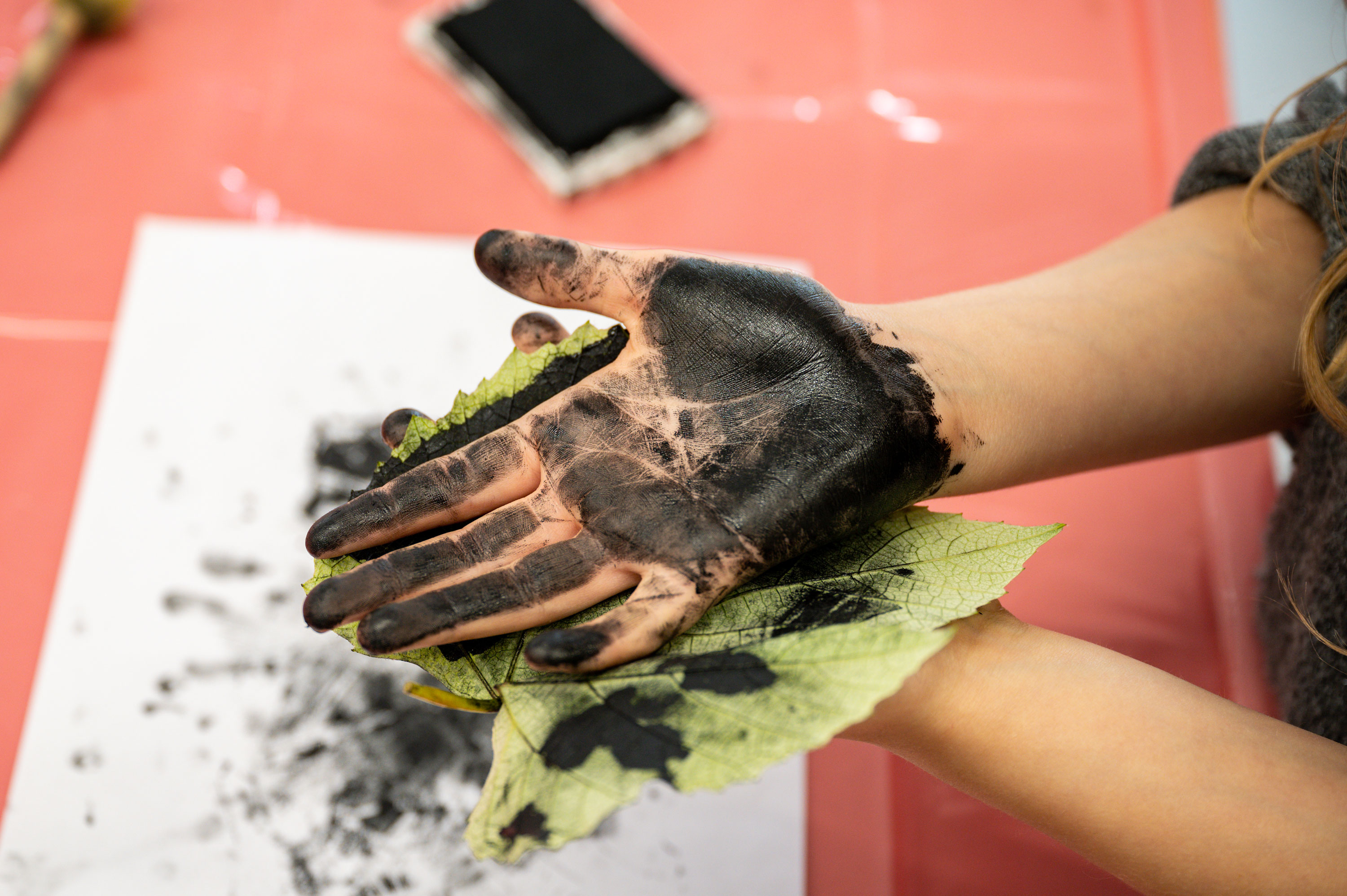 A close-up on a participants hand covered in black ink holding a leaf covered in ink