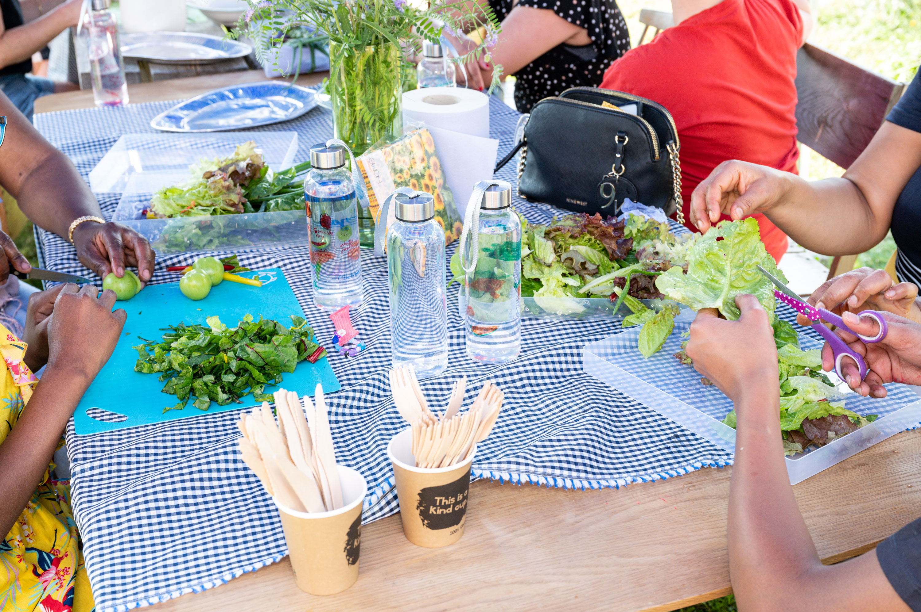 A group of people sitting around a table and using scissors to cut and prepare the salad and limes