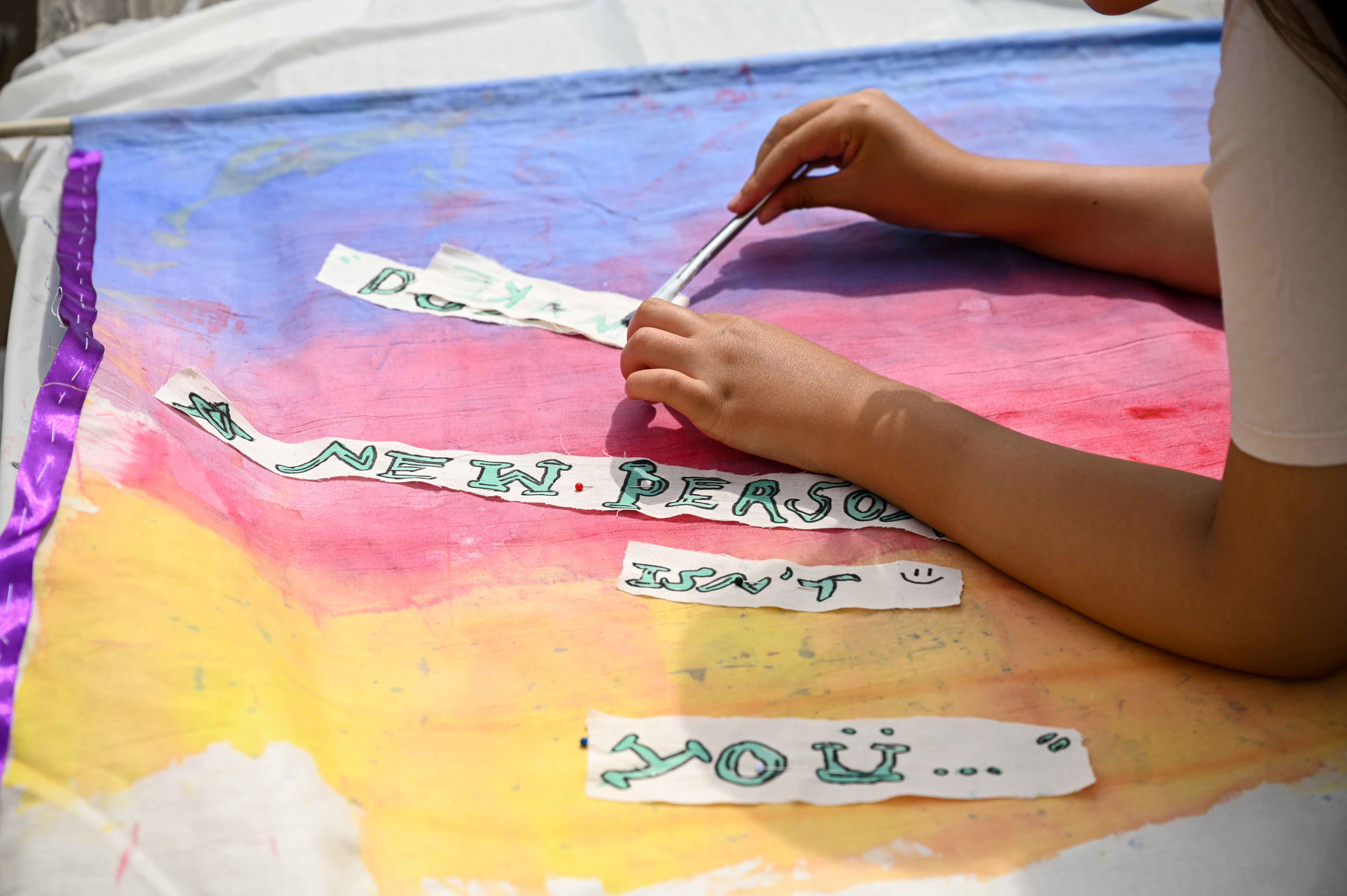 Young person glues lettering to brightly coloured painted fabric