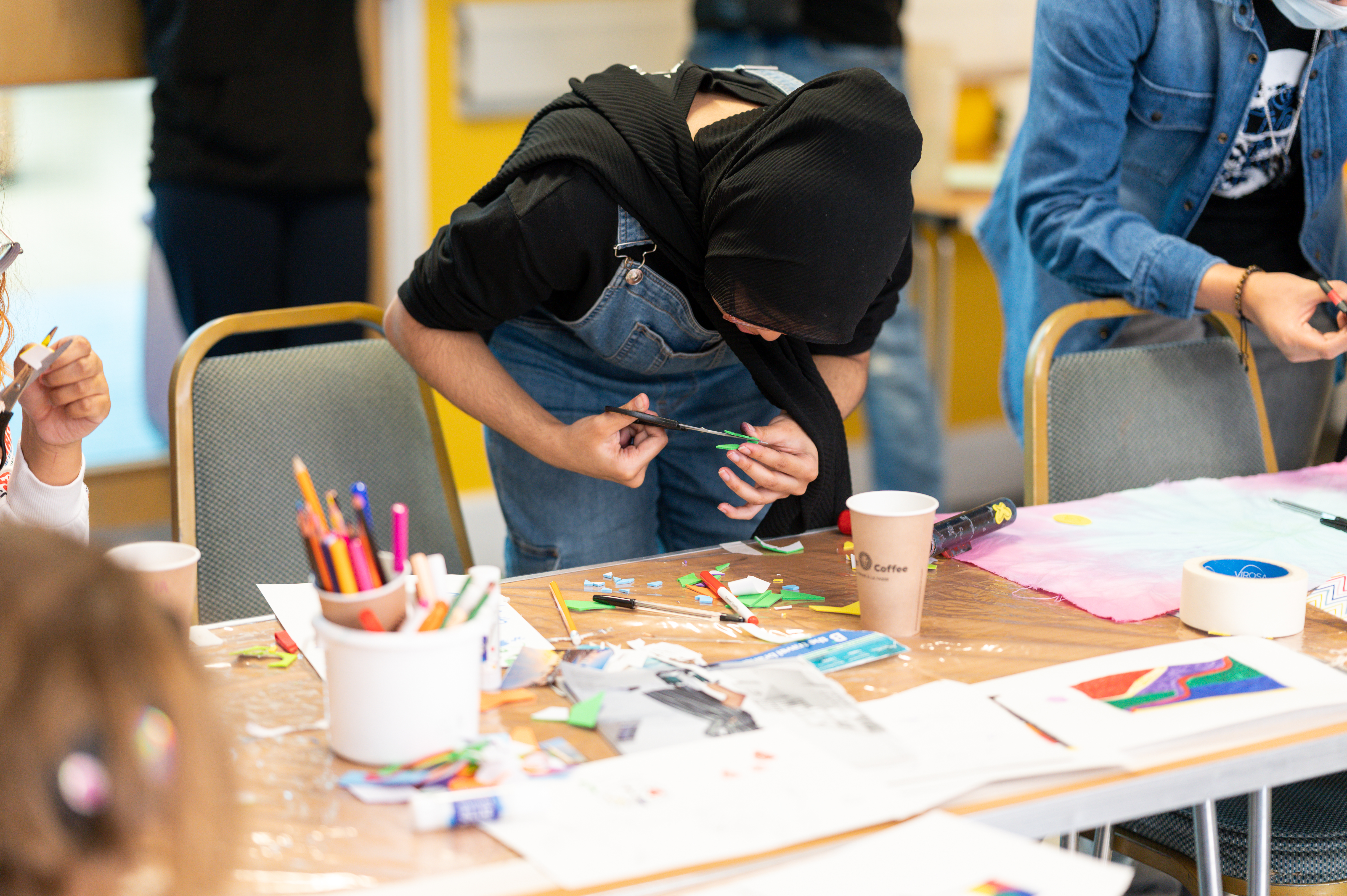 A young person carefully cutting up small pieces of coloured card