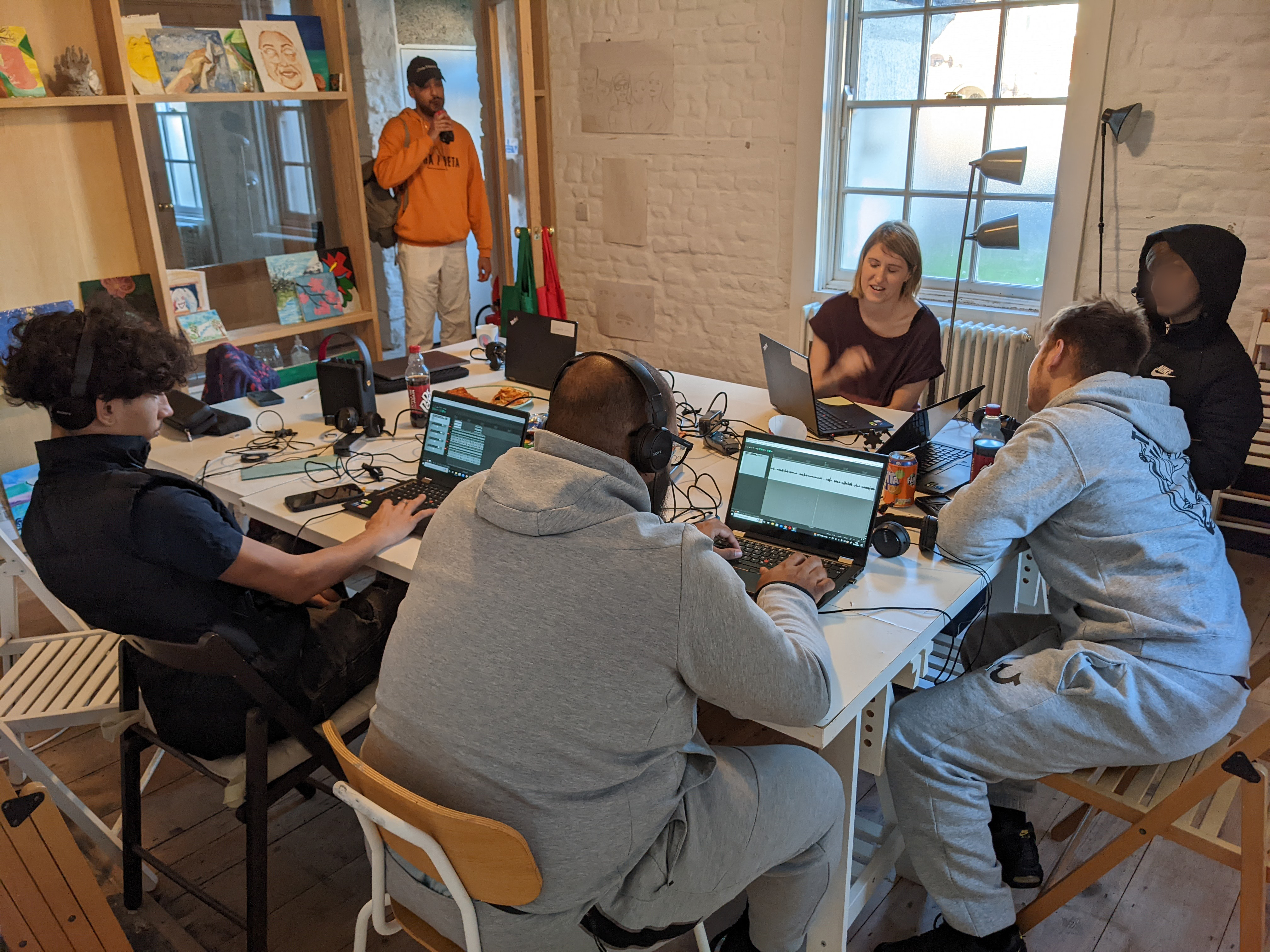 6 people sitting at a table with laptops editing sound