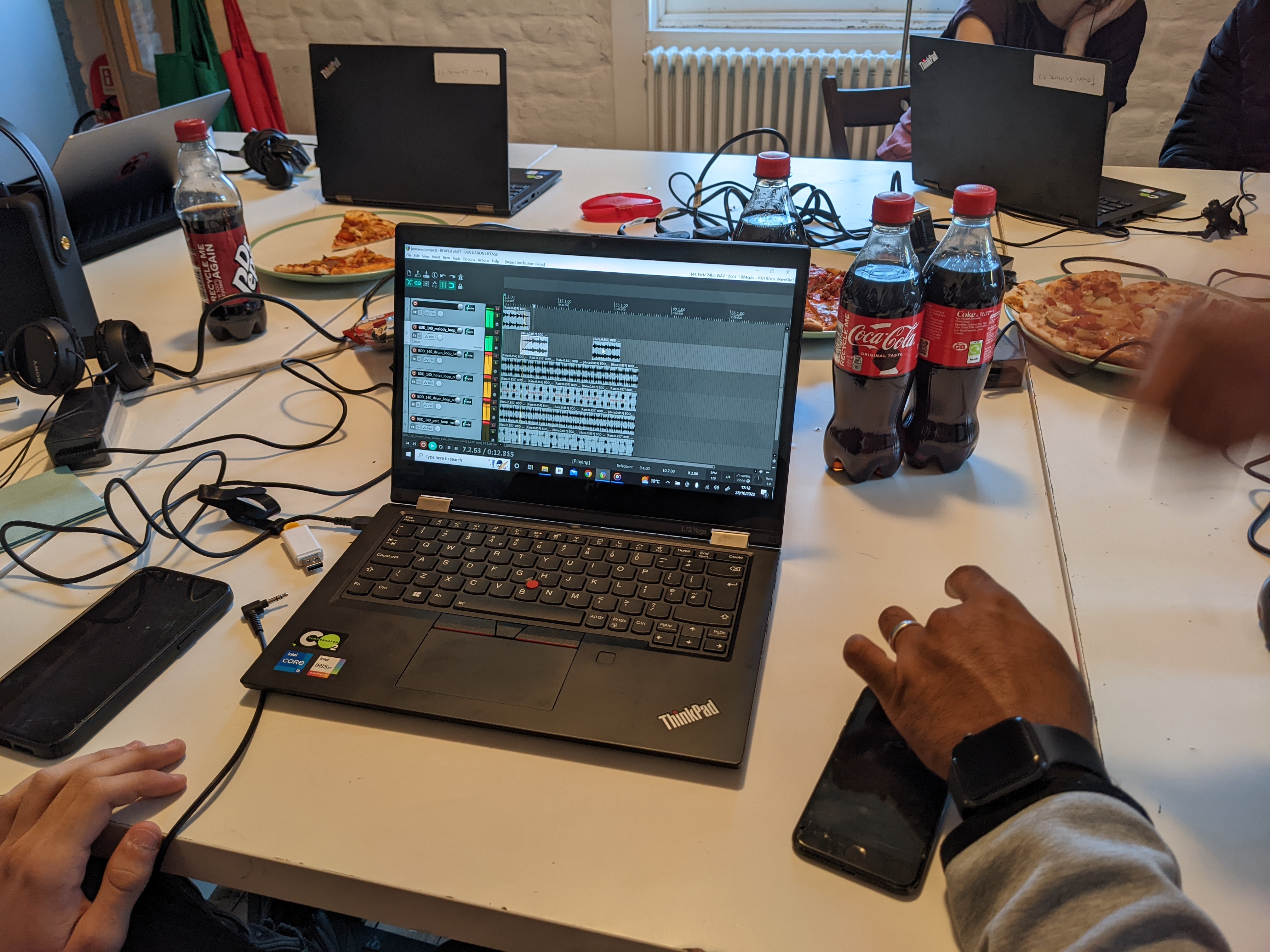 Hands using sound edit software with pizza and cola next to the computer